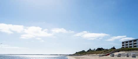 A beach with a clear sky, a sandy shore, and a building with a staircase leading down to the beach.