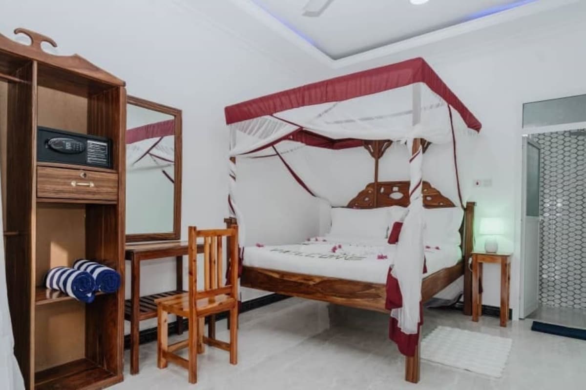 A bedroom with a canopy bed, a wooden wardrobe, a chair, and a bedside table.
