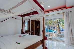 Ein Schlafzimmer mit Baldachinbett, Schreibtisch und Blick auf Pool und Palmen.