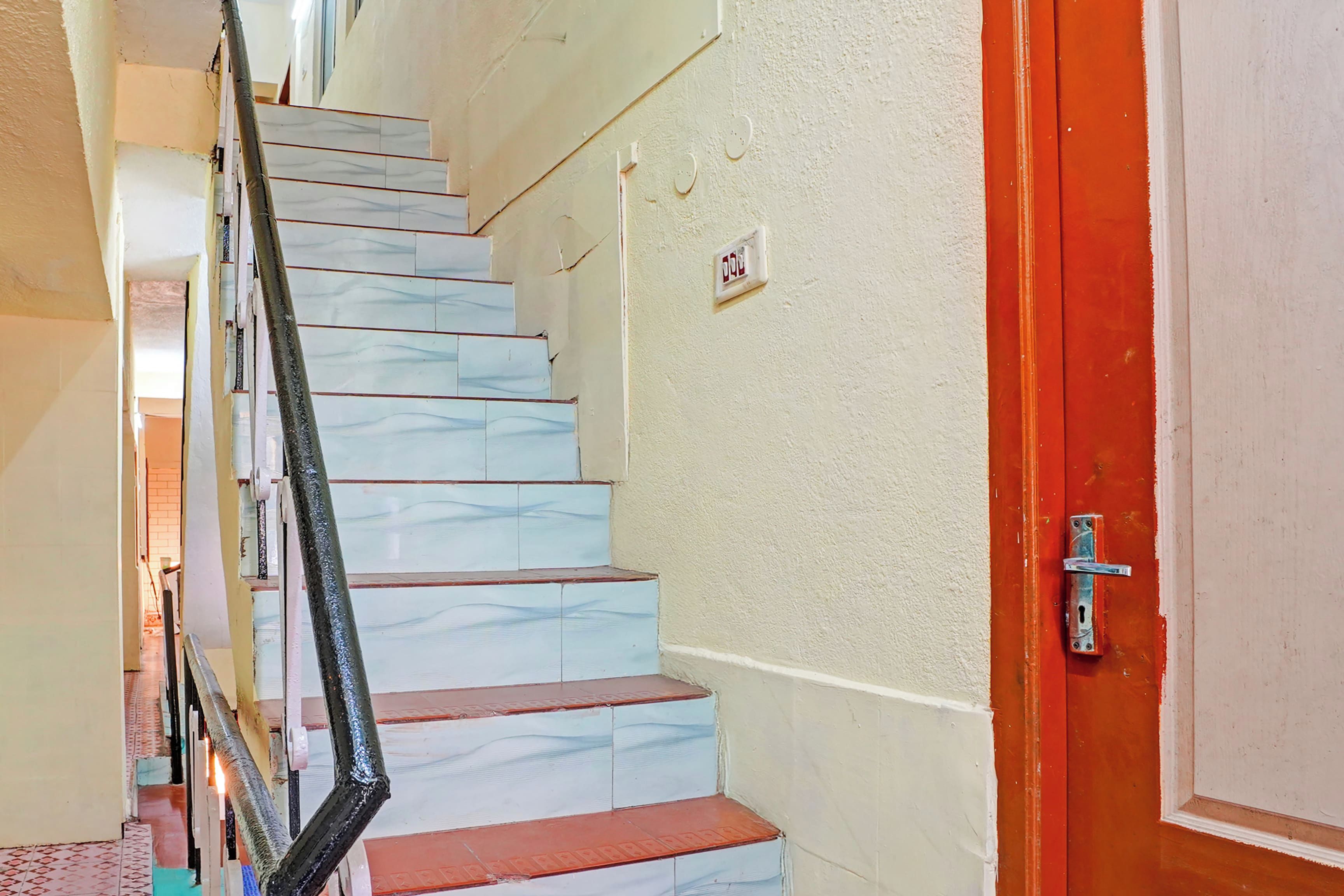 Una escalera con peldaños blancos y rojos, una barandilla metálica y una puerta roja con pomo plateado.