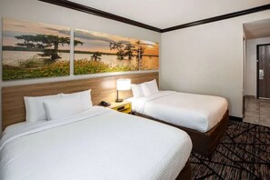 Quarto de hotel com duas camas, uma mesinha de cabeceira com luminária e uma pintura de paisagem grande na parede.