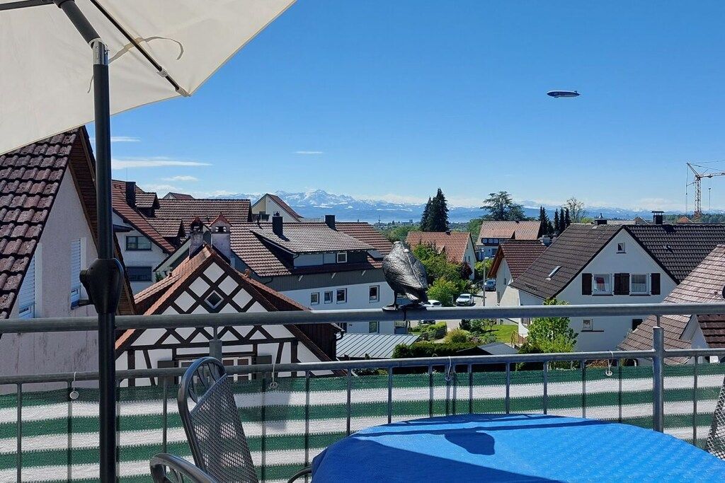 Un balcon donnant sur des maisons, une chaise en métal et un objet bleu posé sur le sol.