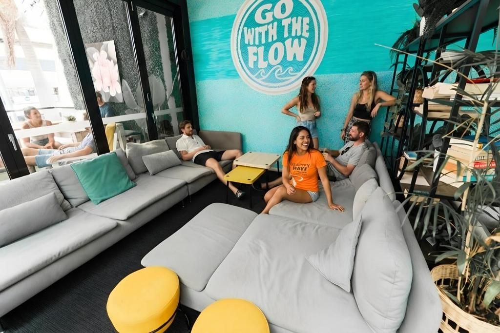 A modern lounge area with a sofa, yellow ottoman, and a wall with a motivational quote.