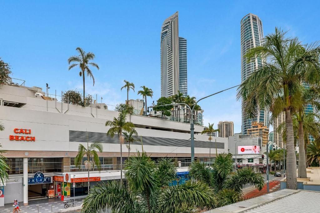 A commercial building with a 'CALI BEACH' sign, palm trees, and high-rise buildings in the background.