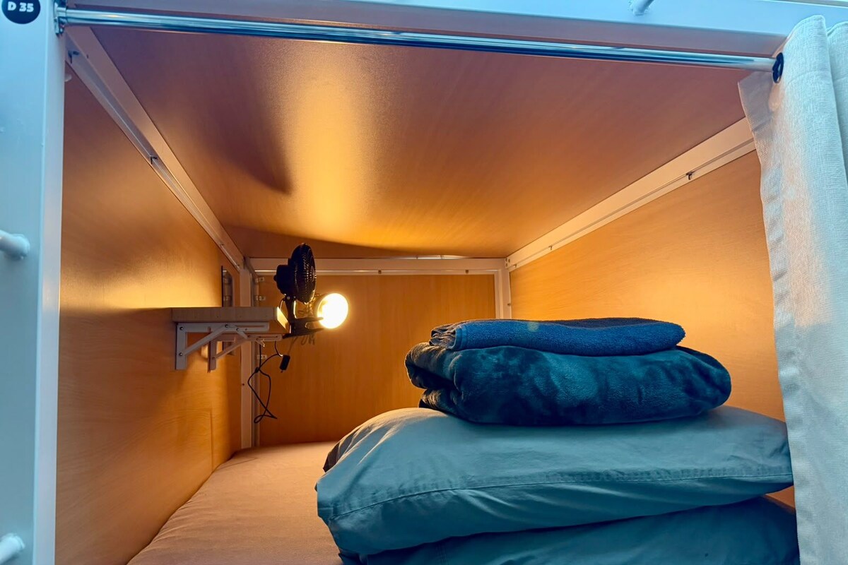 Ett litet rum med en våningssäng, en liten hylla med en fläkt och en lampa.