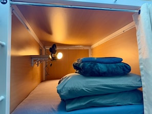 Ett litet rum med en våningssäng, en liten hylla med en fläkt och en lampa.