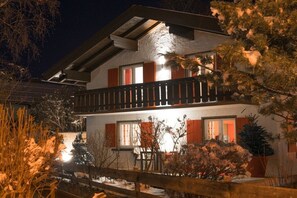A two-story building with a balcony, windows with shutters, and a snow-covered ground.