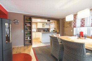 A modern kitchen with a central island, a dining area with wicker chairs, and a red accent wall.