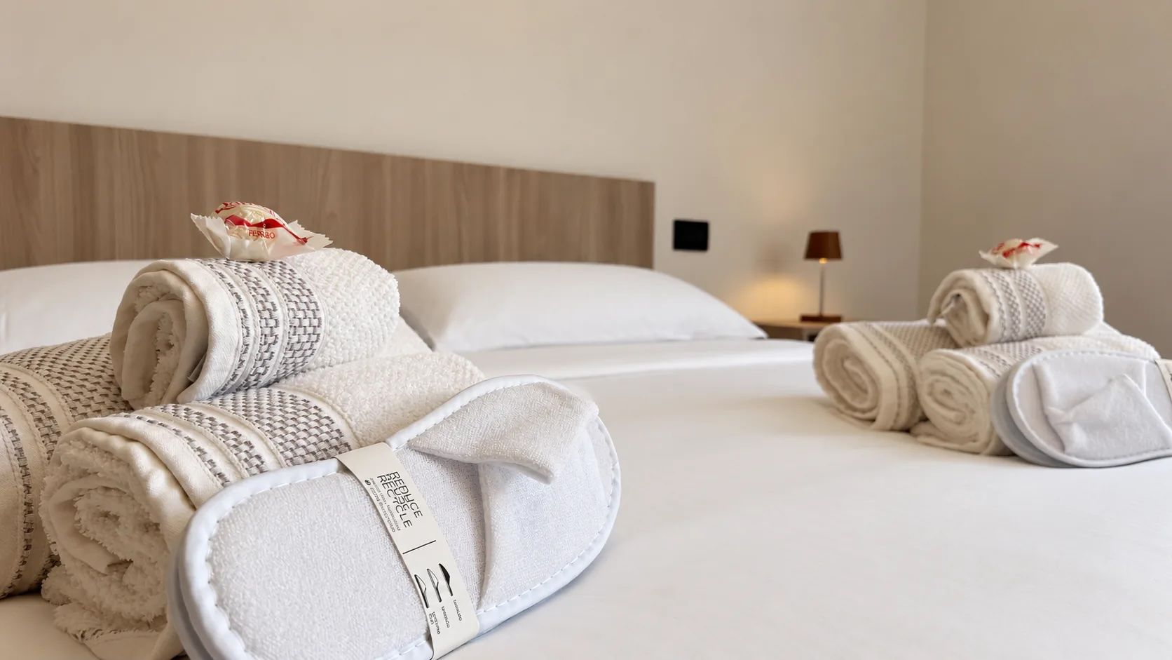 A hotel room with neatly folded towels, a bed, a nightstand, and a lamp.