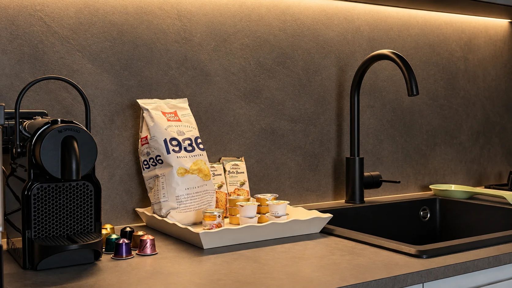 A kitchen counter with a coffee machine, a bag of coffee pods, a sink, and a tray with food items.