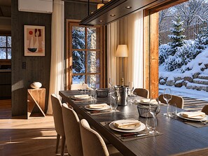 Ein Essbereich mit einem langen Tisch, der für eine Mahlzeit gedeckt ist, Holzwänden und Blick auf eine verschneite Landschaft durch ein großes Fenster.