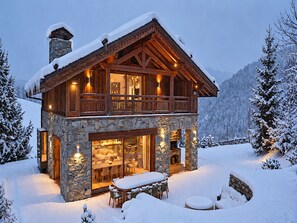 Eine zweistöckige Holzhütte mit Steinunterbau, einem Balkon und einem Essbereich mit Außenbestuhlung.