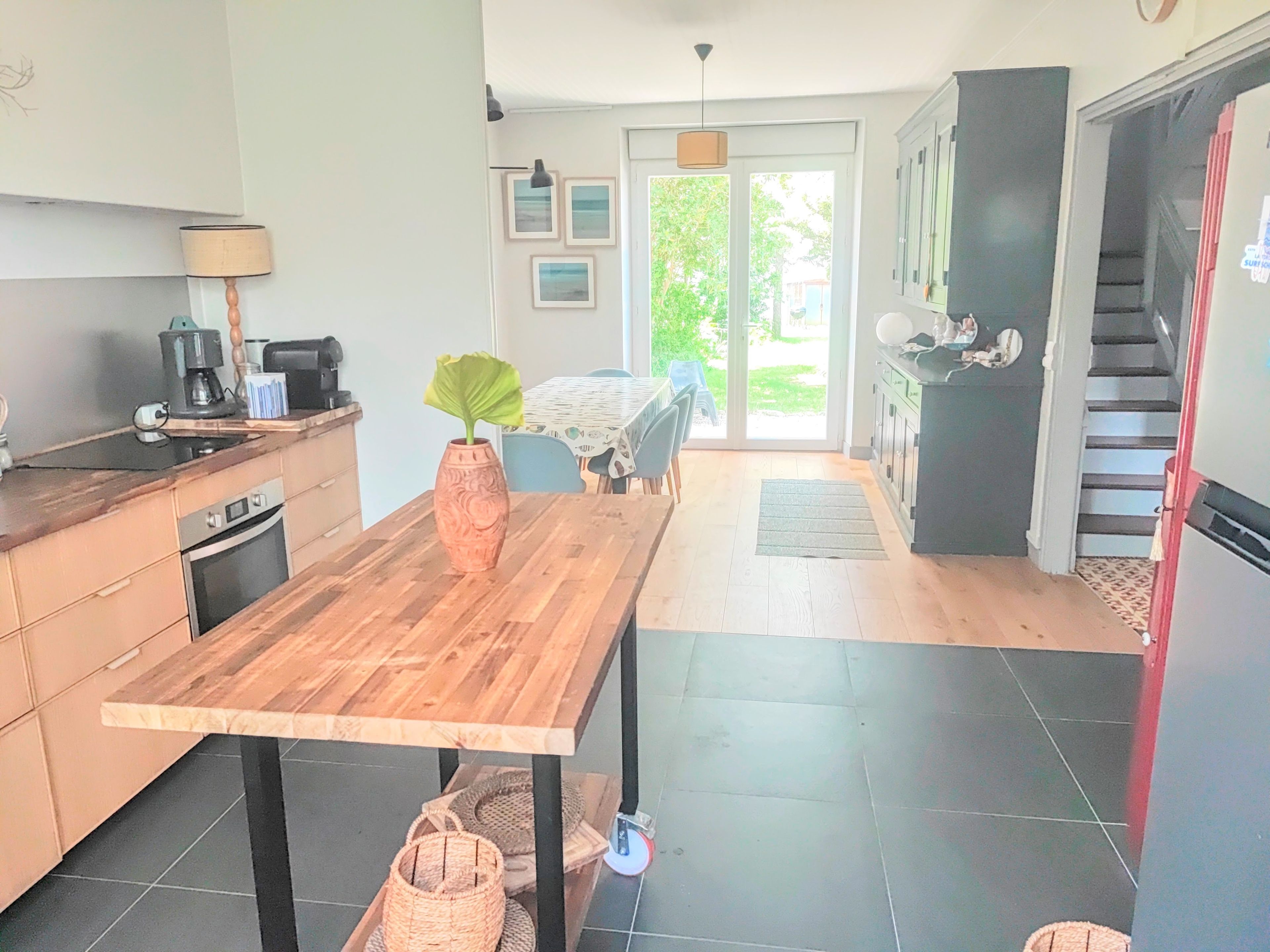 Una cocina con una mesa de madera, un florero con una planta y un comedor con sillas.