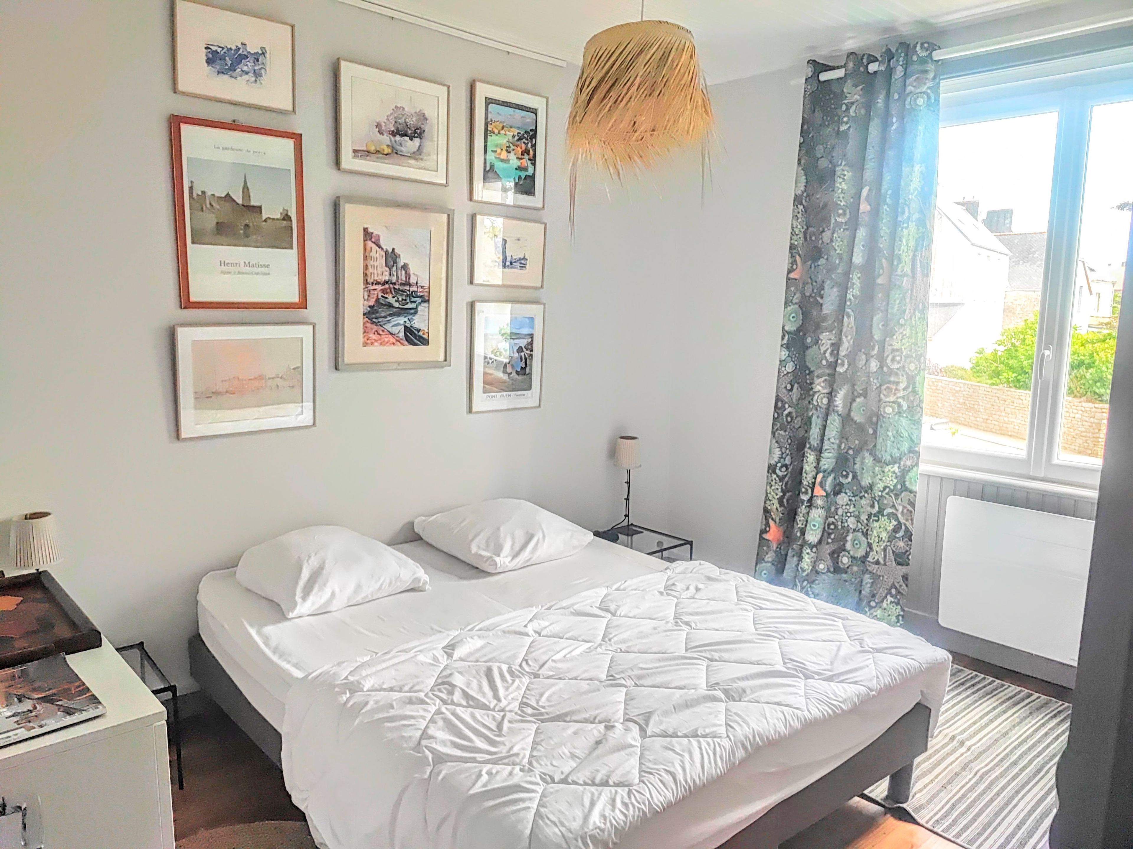 Un dormitorio con cama, mesita de noche, lámpara y ventana con cortinas.