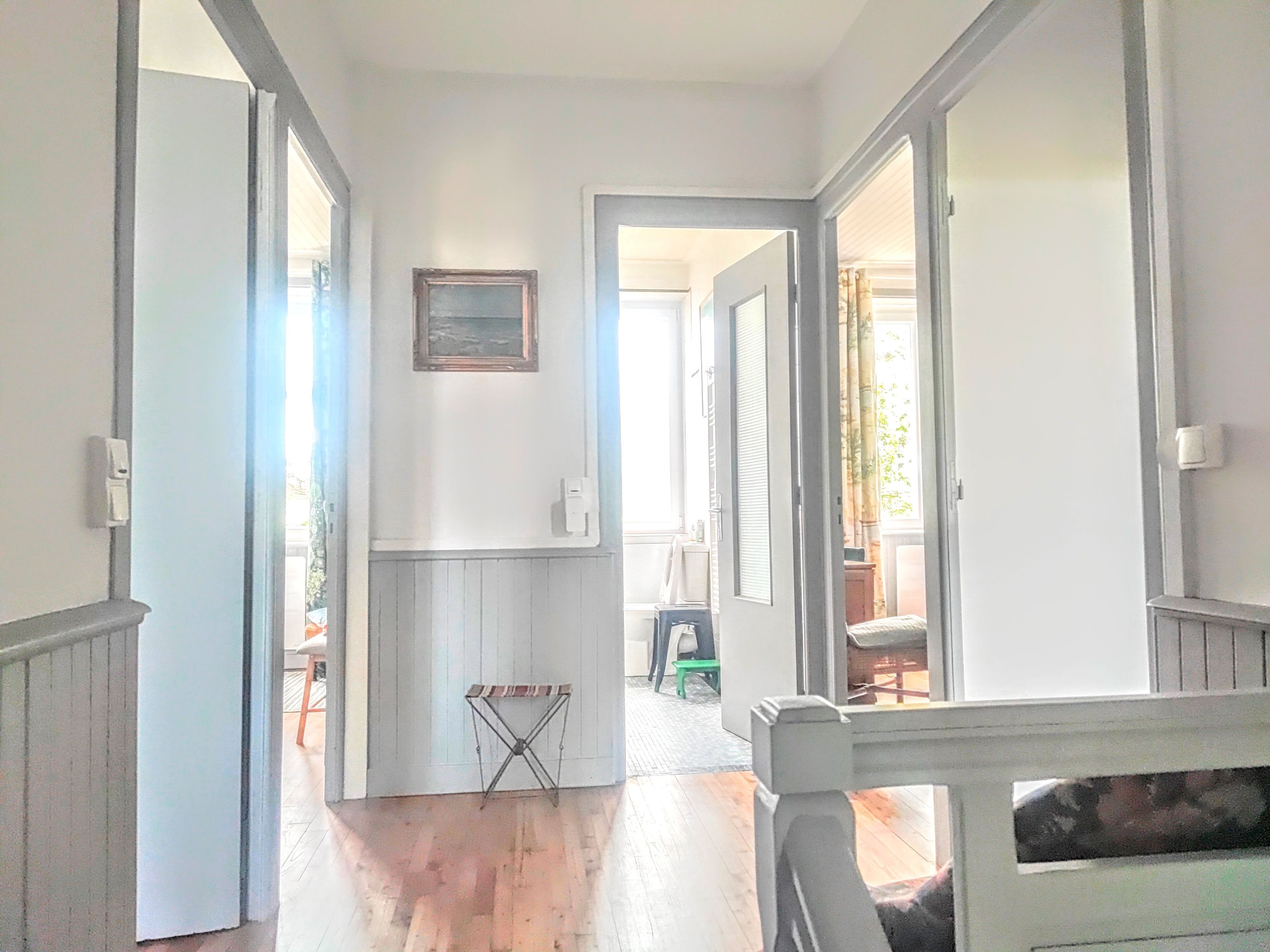 Un pasillo con piso de madera, paredes blancas y una puerta que da a otra habitación.