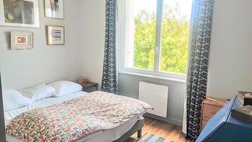 Un dormitorio con una cama, una mesita de noche, un radiador, una ventana con cortinas y una obra de arte en la pared.