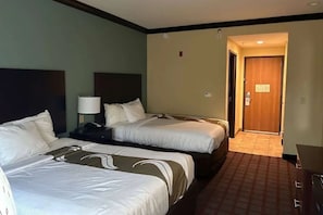 Una habitació d'hotel amb dos llits, una tauleta de nit, una làmpada i una porta que dona a una altra habitació.