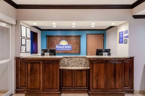 Un comptoir d’accueil orné du logo de Days Inn, un comptoir en bois et un mur d’accent bleu.