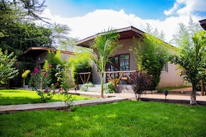 Una casa de dos pisos con un porche cubierto, rodeada de exuberante follaje y plantas florecientes.