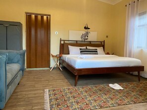Un dormitorio con una cama de madera, un sofá azul, un tapete estampado y una puerta a rayas verticales.