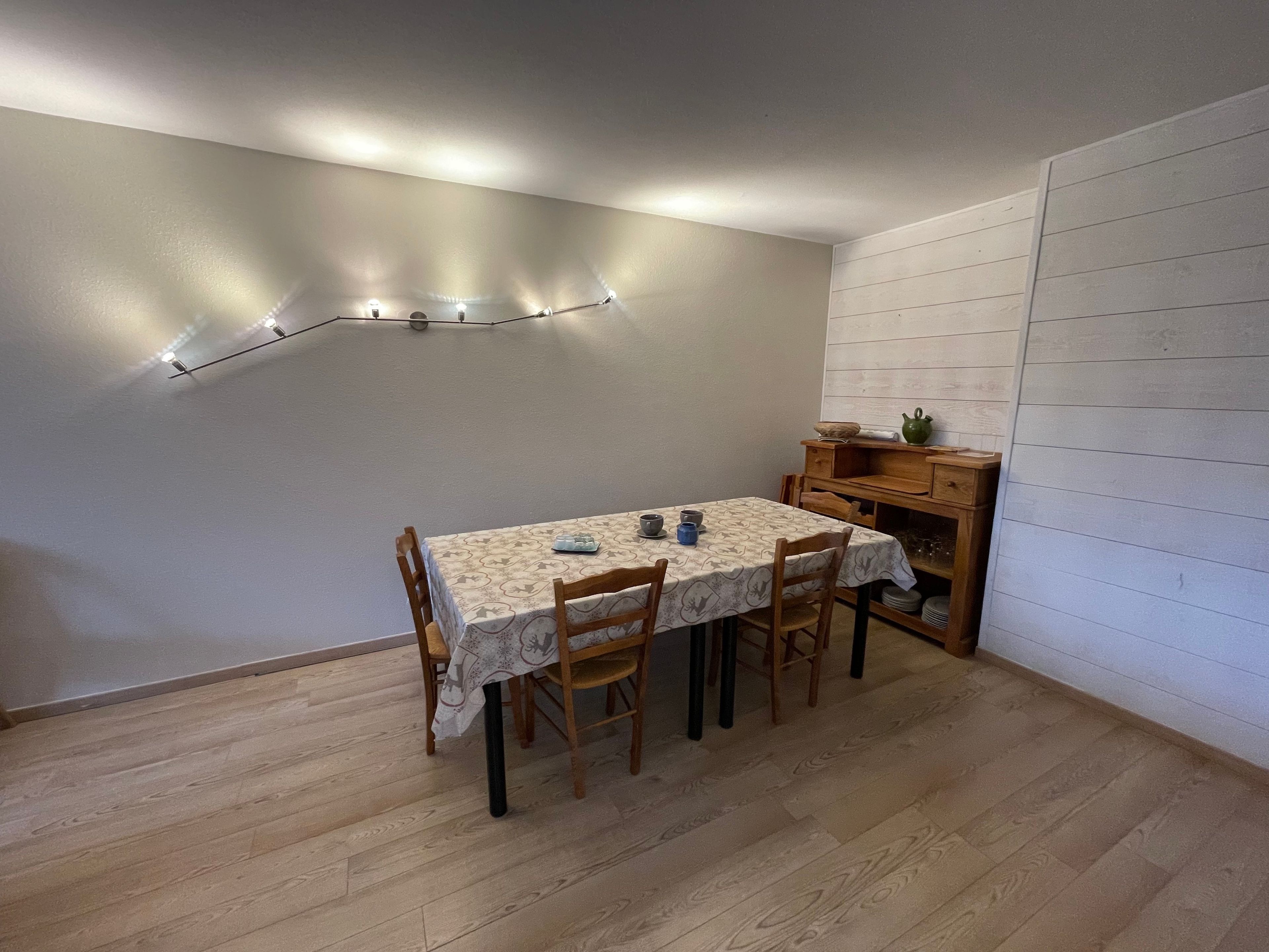 Un área de comedor con una mesa, sillas y una lámpara fijada a la pared.