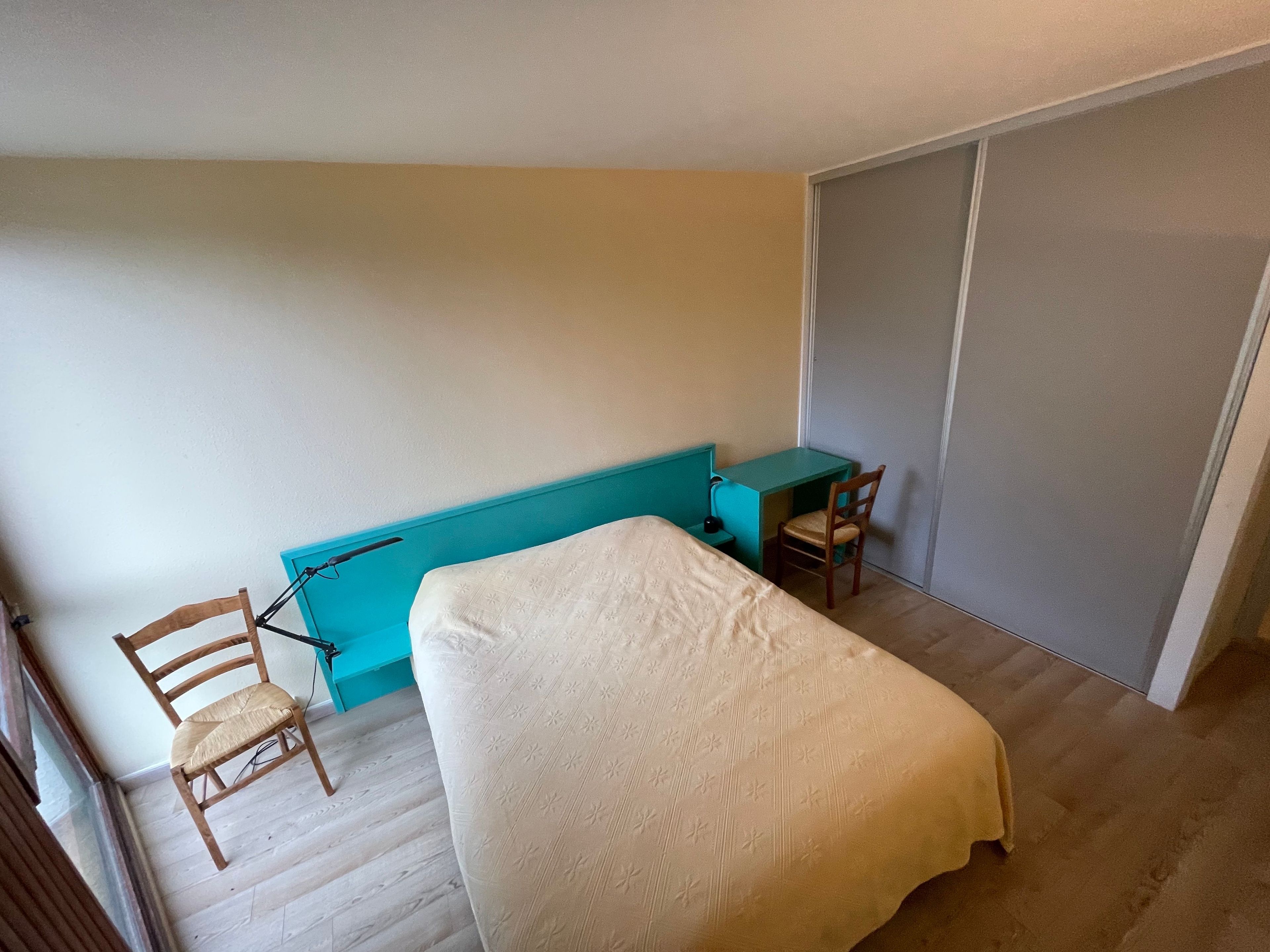 Una habitación pequeña con cama individual, escritorio, silla, armario y ventana.