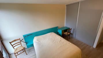 Una habitación pequeña con cama individual, escritorio, silla, armario y ventana.