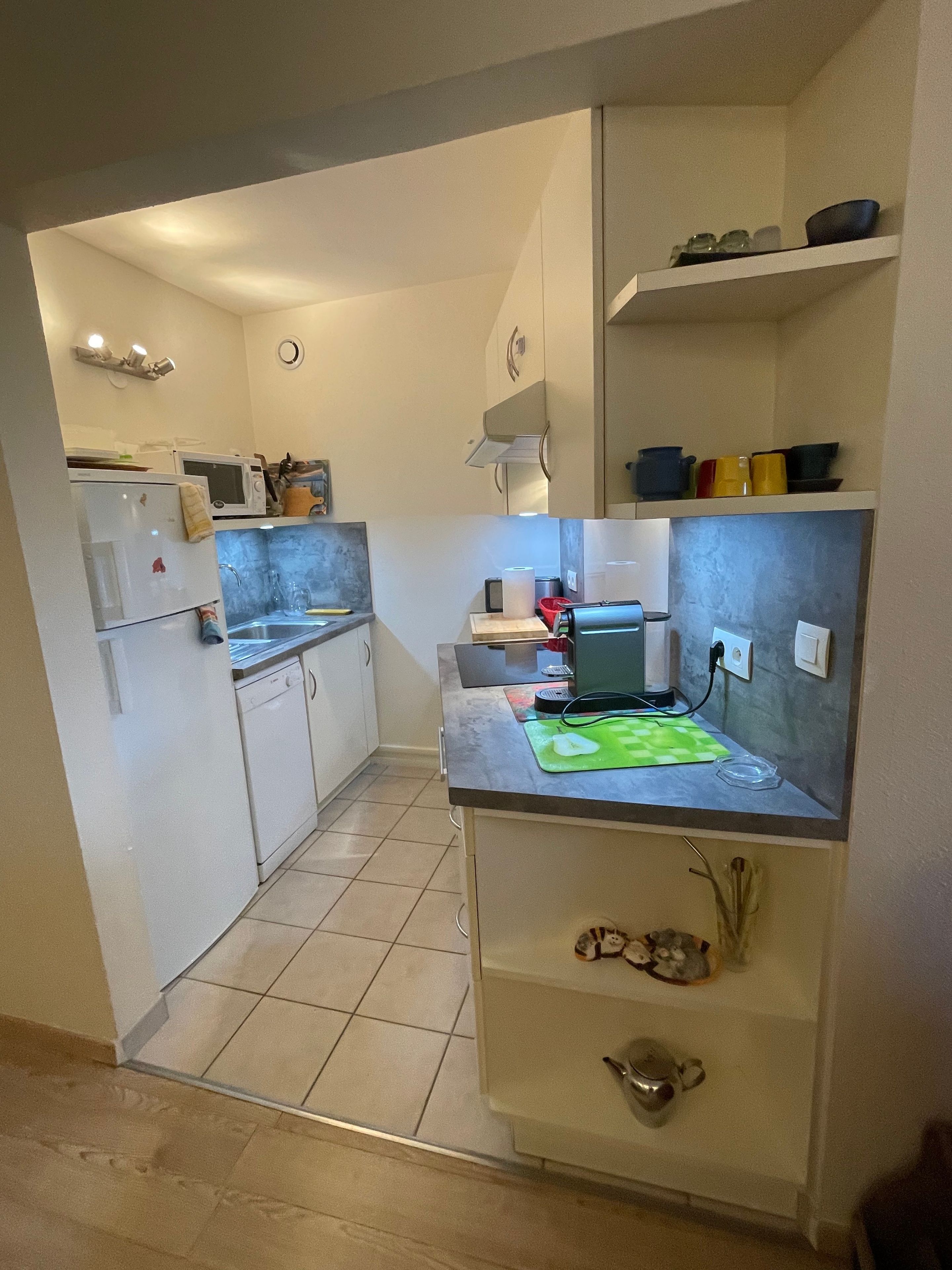 A compact kitchen with a microwave, refrigerator, and a small countertop with a kettle and a kettle holder.