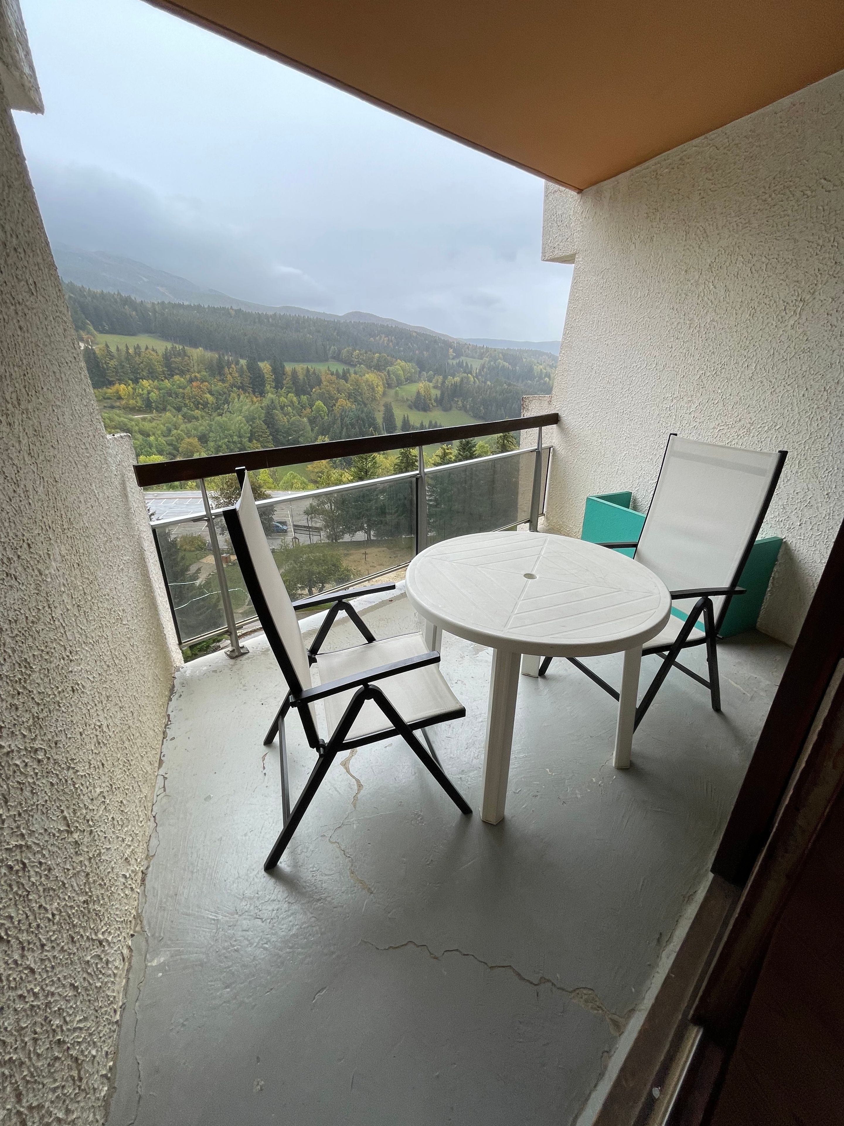 A balcony with a white table and chairs, a view of a green landscape, and a whiteboard.