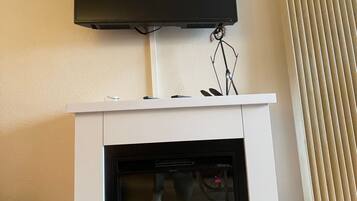 Una chimenea con un televisor montado encima, una silla y una ventana con persianas.