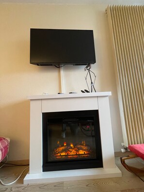 Una chimenea con un televisor montado encima, una silla y una ventana con persianas.