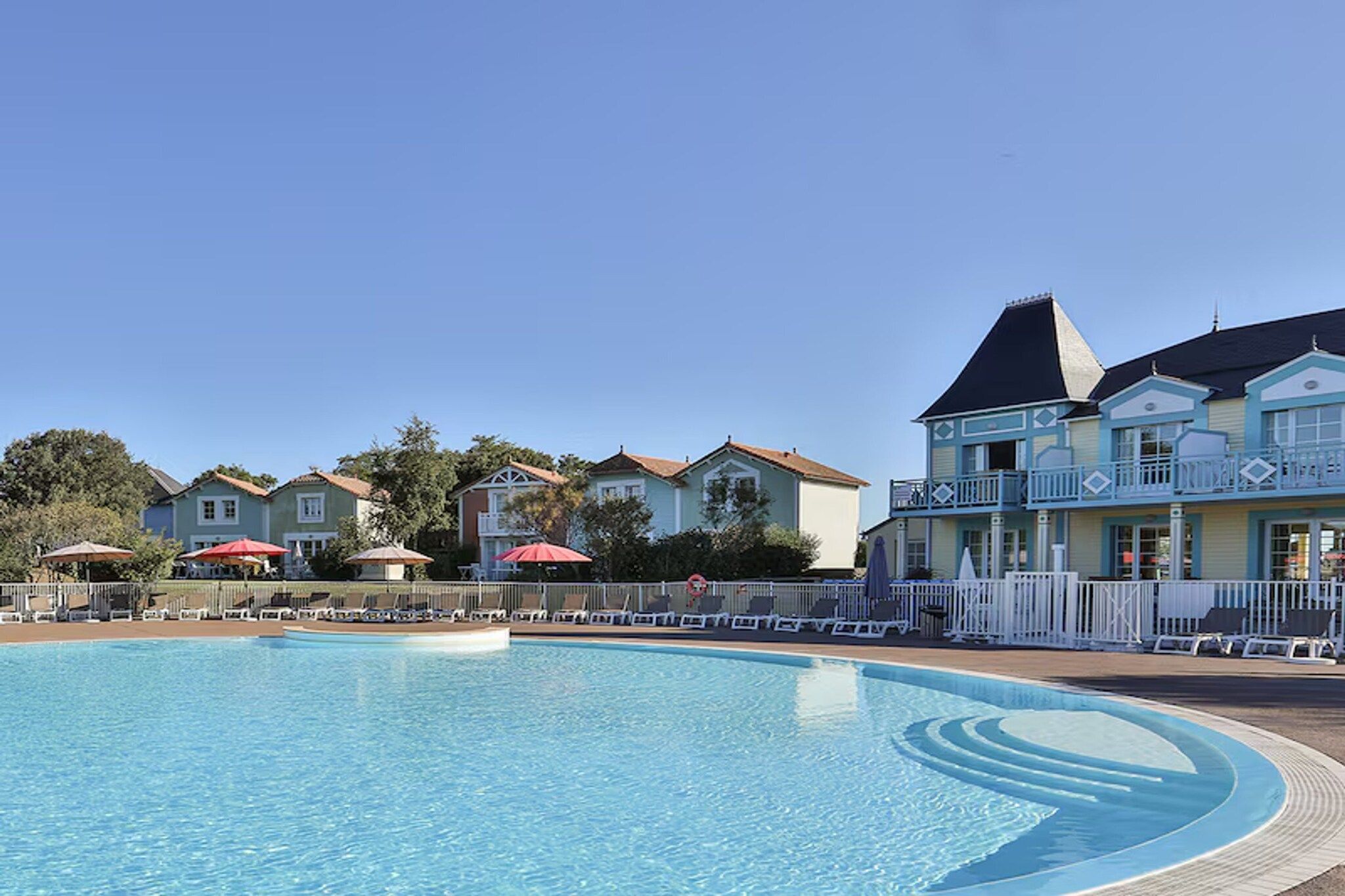 Une piscine entourée de maisons dotées de balcons, avec des chaises longues et des parasols à proximité.