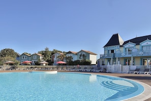 Une piscine entourée de maisons dotées de balcons, avec des chaises longues et des parasols à proximité.