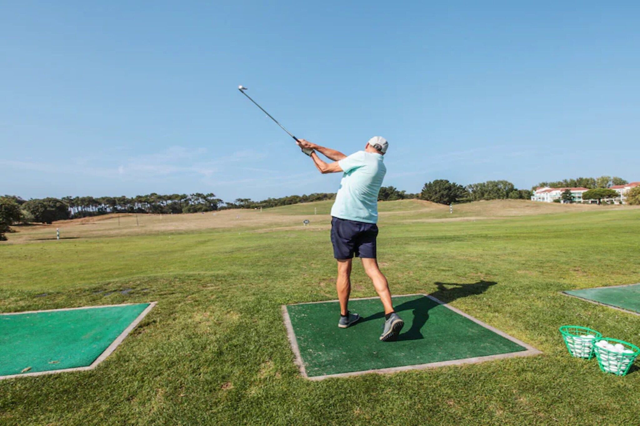 Eine Person schwingt auf einer Übungsfläche einen Golfschläger, während sie auf einer grünen Matte steht.