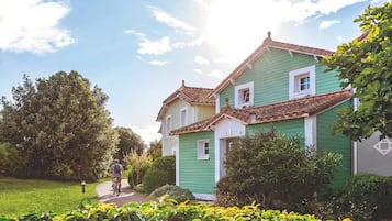 Una casa verde con tetto in tegole, circondata dal verde e da un cielo sereno.