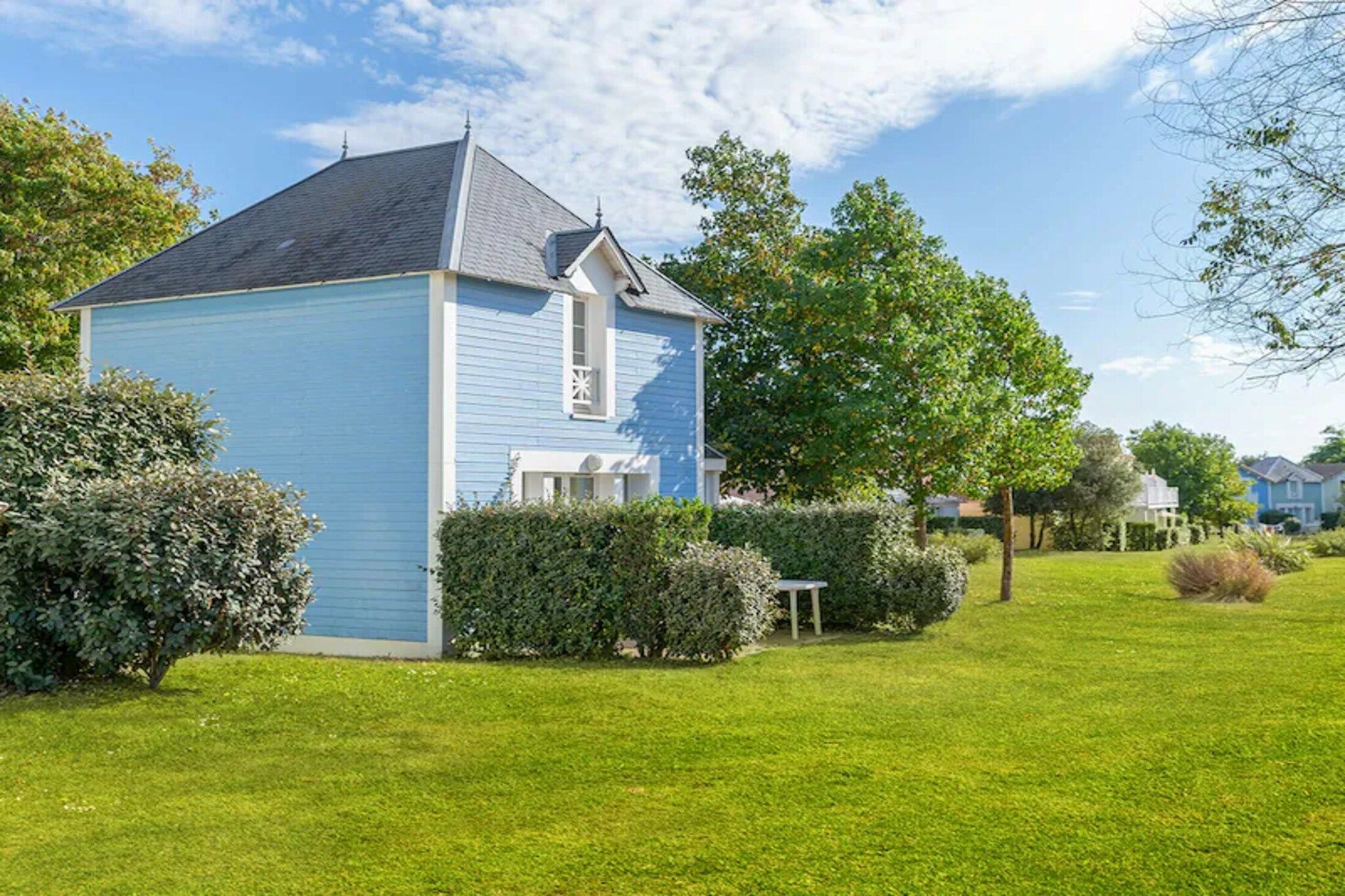 Une maison de plain-pied avec un toit à pignon, entourée d’une pelouse bien entretenue et de divers arbustes.