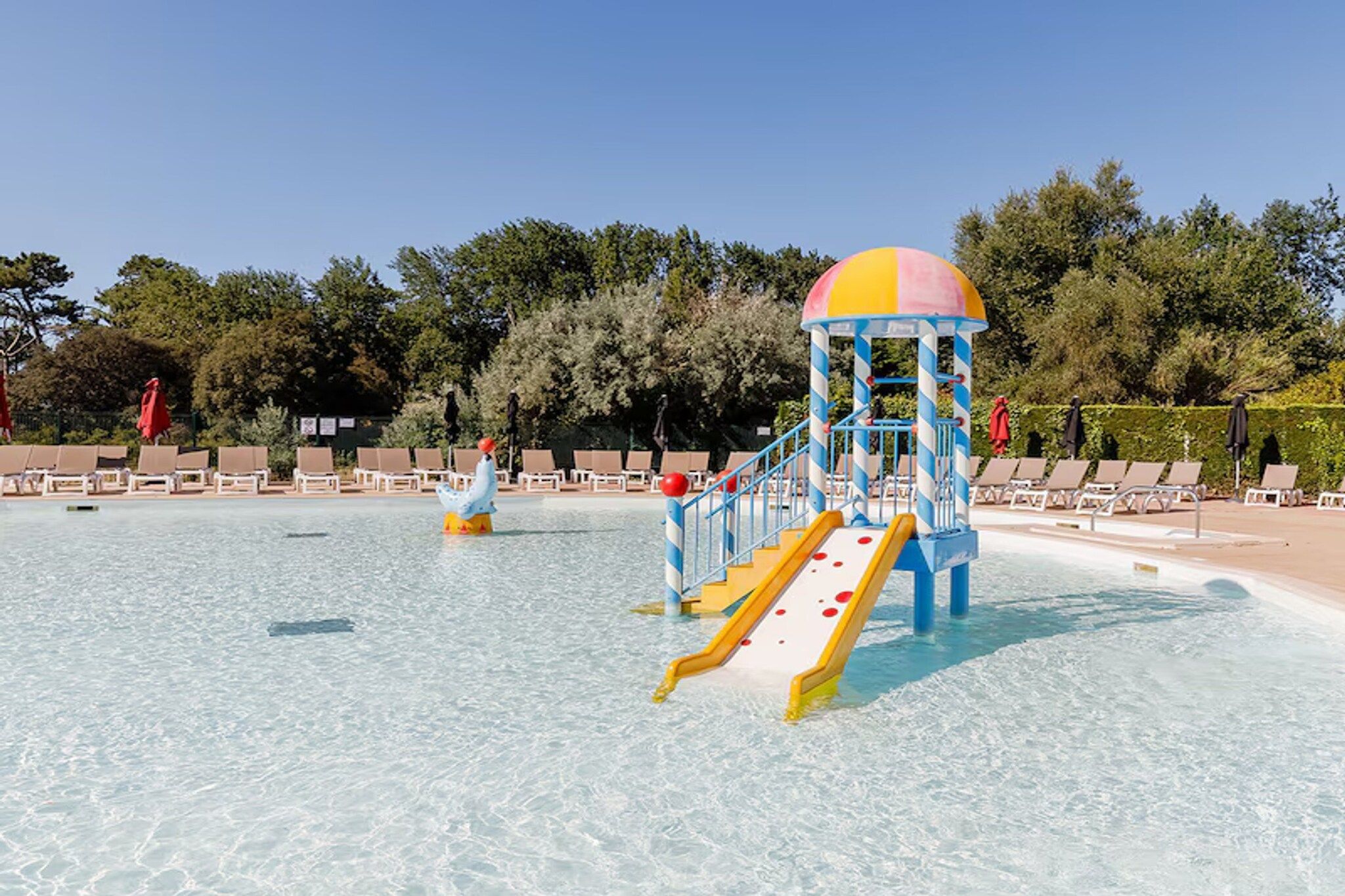 A water park with a slide structure, clear shallow water, and lounge chairs.