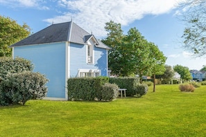 Een gelijkvloers huis met een puntig dak, omgeven door een verzorgd gazon en diverse struiken.