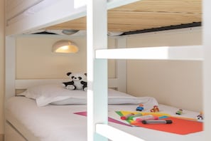 Een slaapkamer met een stapelbed, een panda-knuffel op het onderste bed, een wandlamp en kinderspeelgoed op het bed.