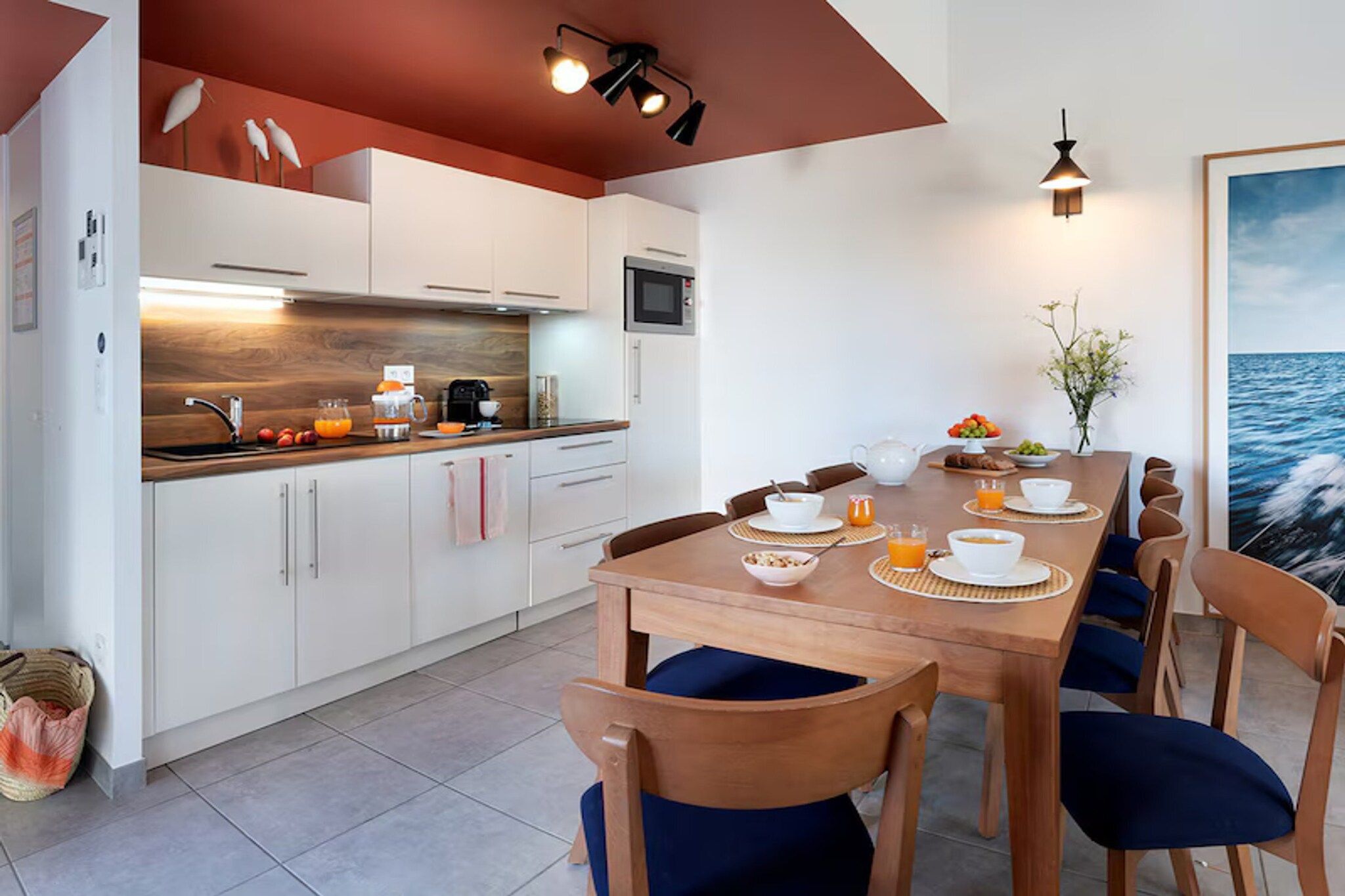 A modern kitchen with white cabinets, a wooden countertop, and a dining area with a wooden table and blue chairs.