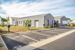 Un bâtiment moderne doté d’un espace d’accueil, de places de stationnement clairement délimitées et offrant une vue sur un ciel dégagé.