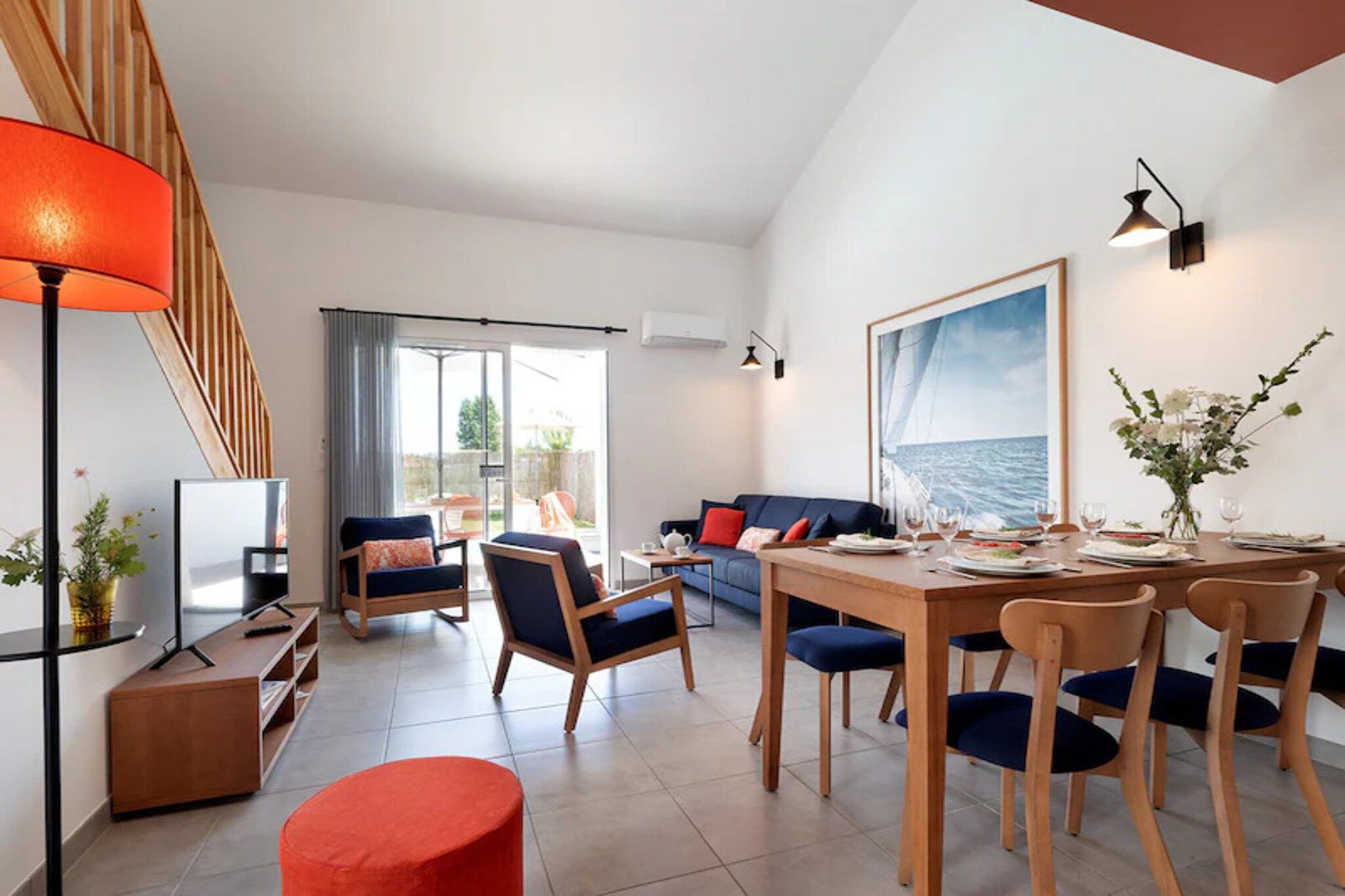 A modern living room with a dining area, a staircase, and a large window with a view.