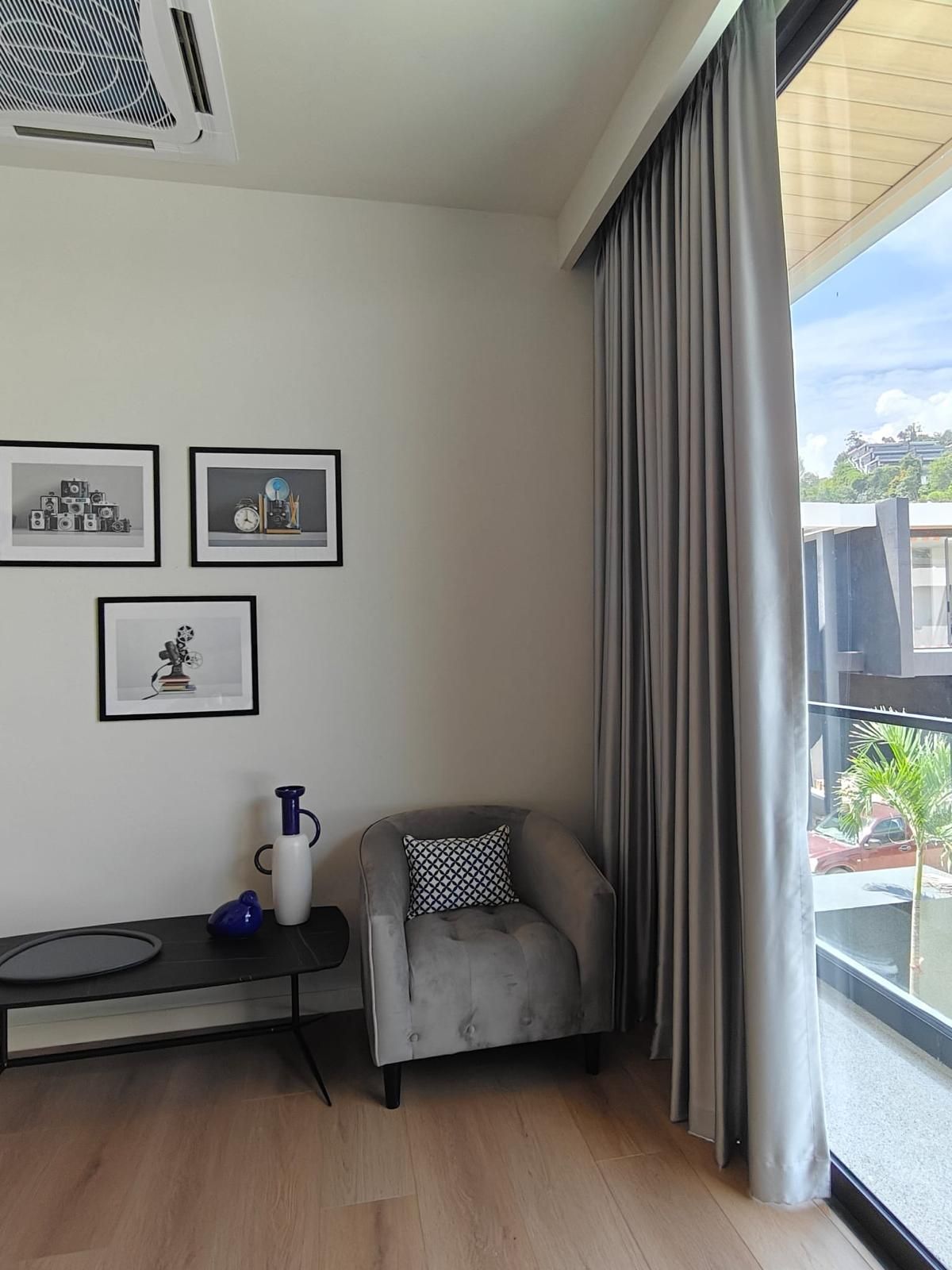 Een moderne woonkamer met een grijze bank, een klein tafeltje met een blauwe vaas, en drie ingelijste foto's aan de muur.