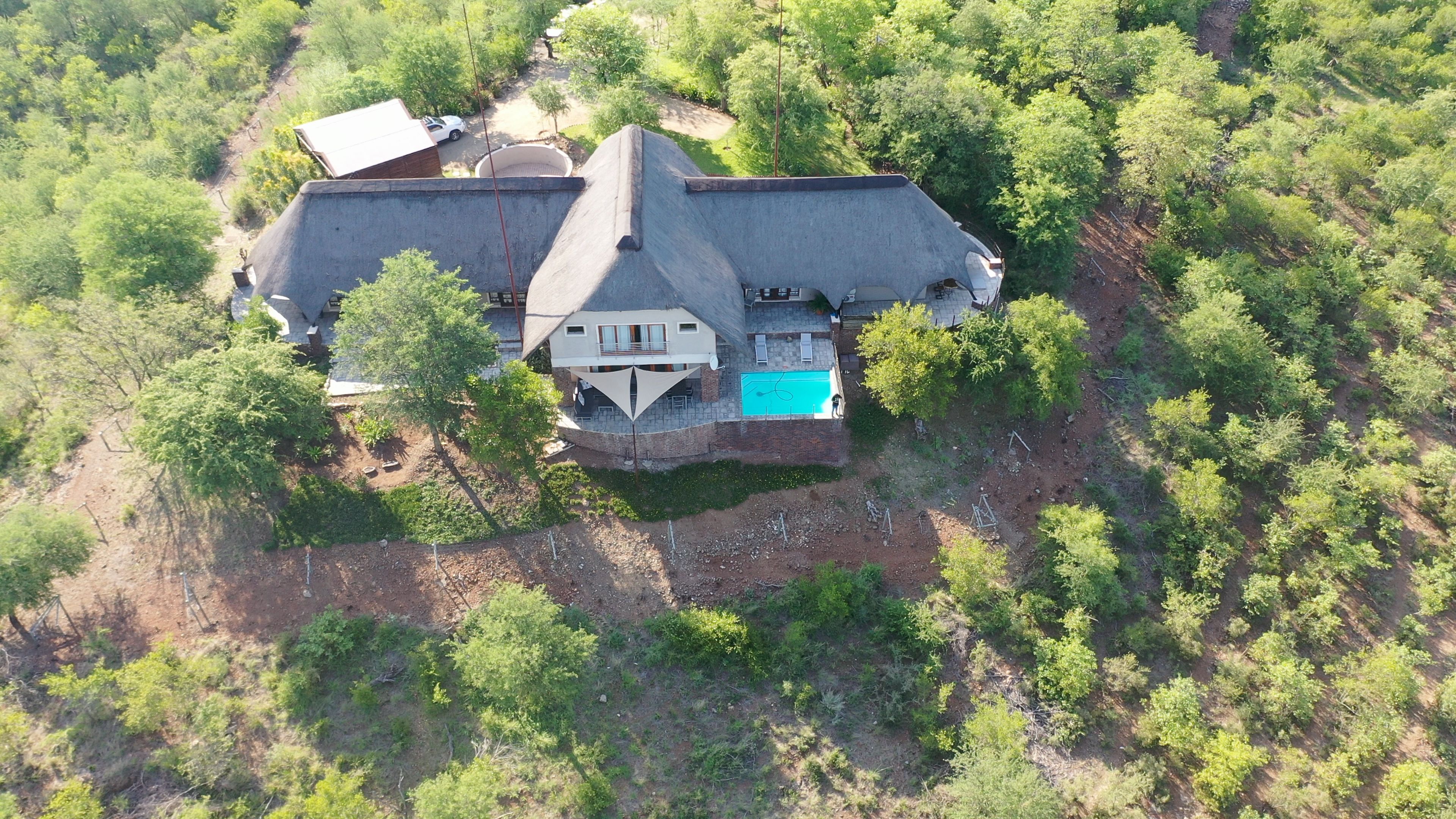 An aerial view of a house with a swimming pool, surrounded by dense greenery.