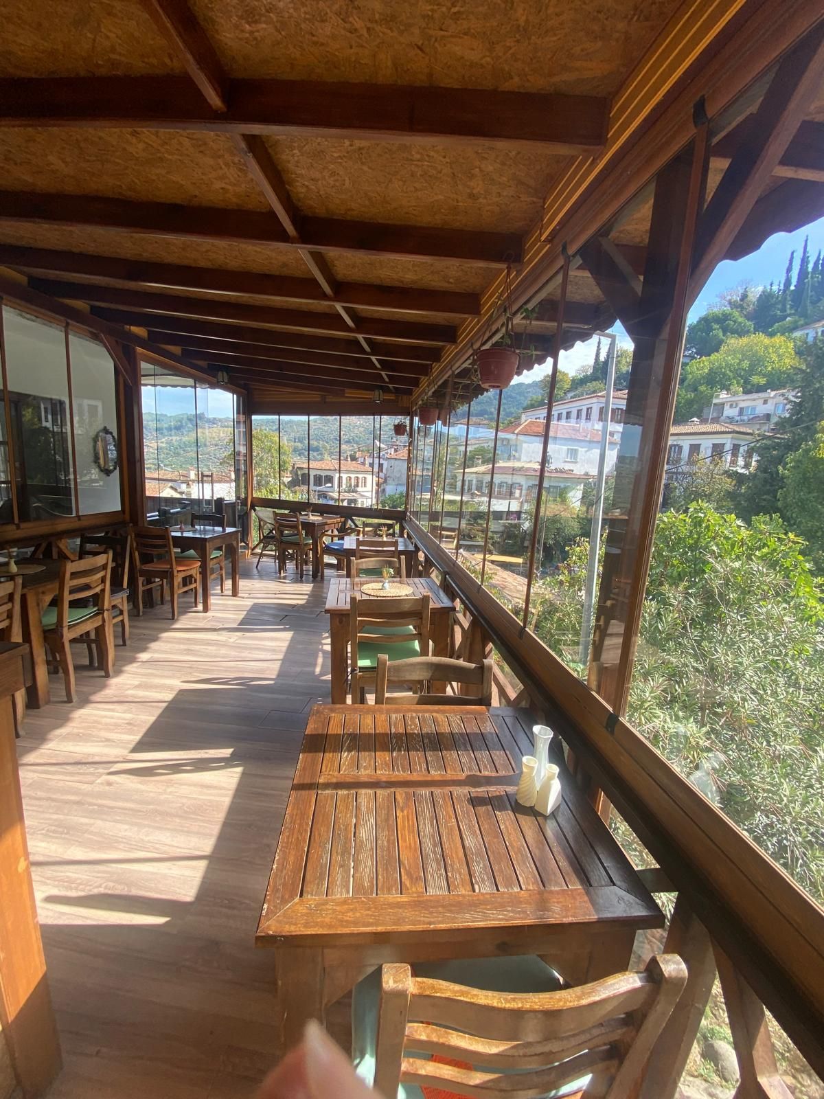 Um deck de madeira ao ar livre com mesas e cadeiras, com vista para uma colina panorâmica.