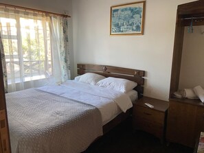 Quarto com cama, mesa de cabeceira, espelho e janela com cortinas.