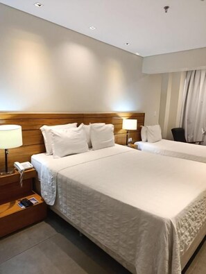 Una habitación de hotel con una cama grande, mesitas de noche, una lámpara y un teléfono.
