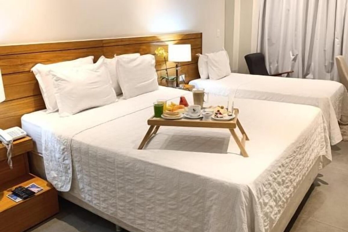 Habitación de hotel con dos camas, cabecero de madera, mesitas de noche con lámparas y una bandeja con alimentos para el desayuno.