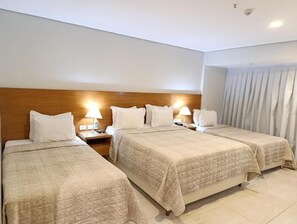 Habitación de hotel con dos camas, cabecero de madera, lámparas de noche y una ventana con cortinas.