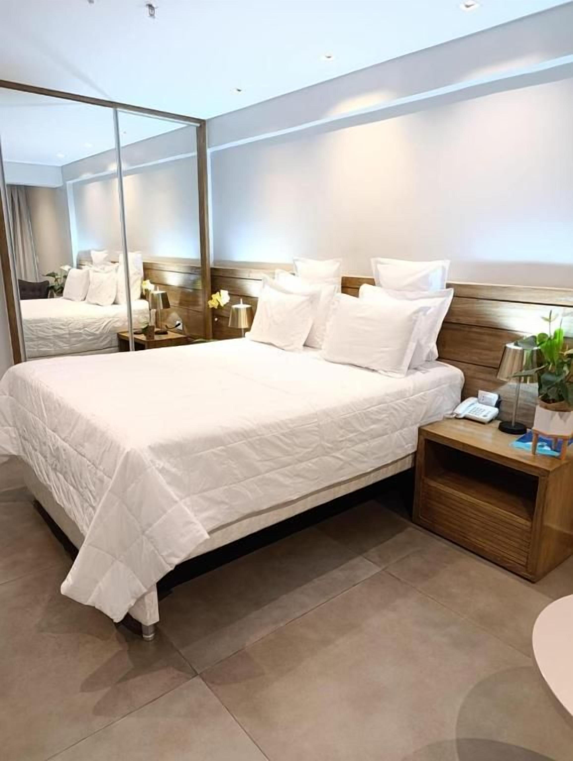 A hotel room with a large bed, a bedside table with a lamp, and a mirror.